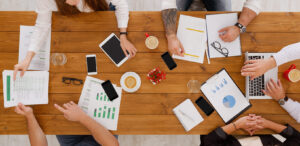 Pessoas de agência de marketing trabalhando com vários papeis, celulares e notebook em cima de uma mesa
