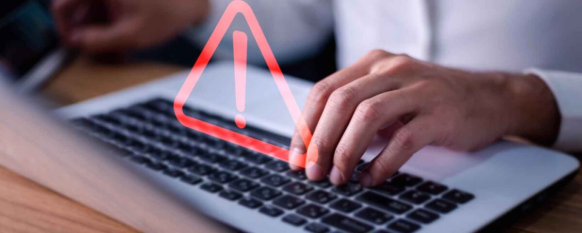 Pessoa mexendo em notebook e sinal de alerta por causa de cuidado com falsas informações