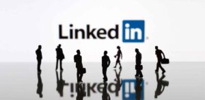 Pessoas com roupas de trabalho, de executivos, andando, e no fundo o logo do LinkedIn