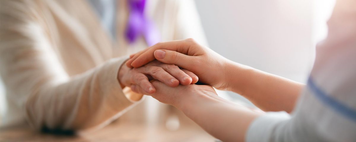 Mulher com laço roxo sendo pega com as mãos de outra pessoa