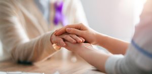 Mulher com laço roxo sendo pega com as mãos de outra pessoa